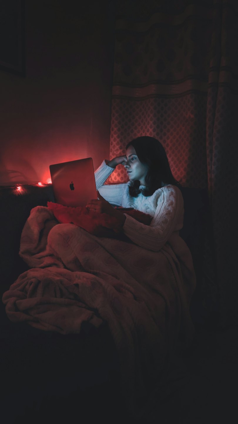 Woman working on a laptop while wrapped in a blanket.