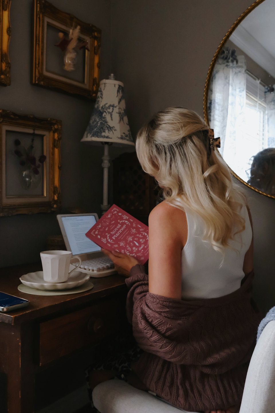 Woman reading a pink book at a desk with a tablet.